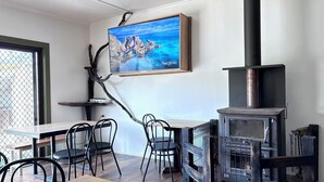 A dining area with a table and chairs, a painting of a coastal landscape, and a wood-burning stove.