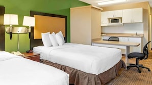 Une chambre d’hôtel avec deux lits, un bureau avec une chaise, un four à micro-ondes et un téléphone sur la table de chevet.