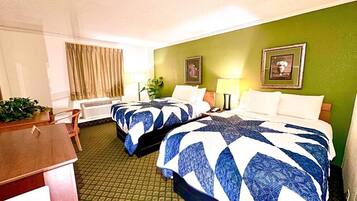 A hotel room with two beds, a desk, a chair, a window with curtains, and a green wall.