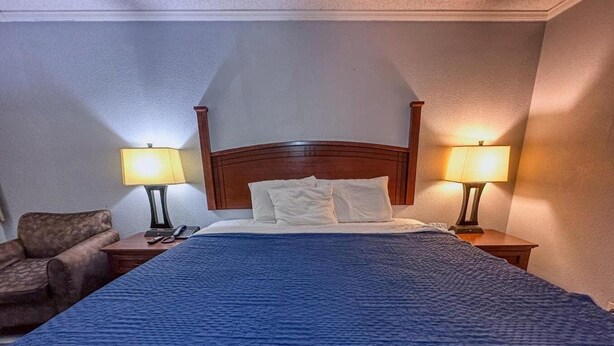 A hotel room with a large bed, two bedside lamps, a chair, and a wooden headboard. - Jacksonville Inn (Jacksonville)