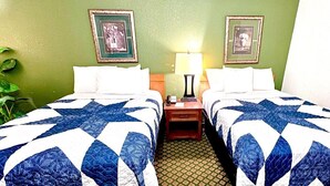 A hotel room with two beds, green walls, framed pictures, a nightstand with a lamp, and a potted plant. - Jacksonville Inn (Jacksonville)