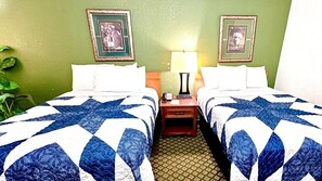 A hotel room with two beds, green walls, framed pictures, a nightstand with a lamp, and a potted plant. - Jacksonville Inn (Jacksonville)