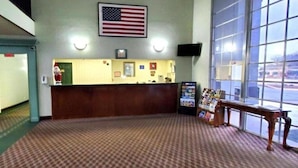A reception area with a check-in counter, an American flag, a clock, and a window with a view of the outside. - Jacksonville Inn (Jacksonville)