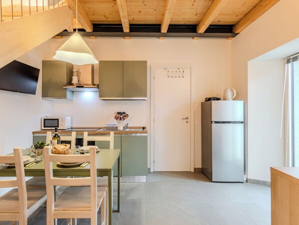 A modern kitchen with a dining area, wooden ceiling beams, and a built-in microwave. - Riflessi by Interhome (Colico)