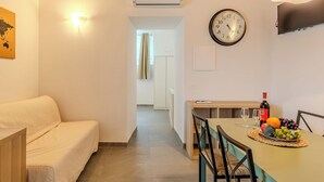 Ein modernes Wohnzimmer mit Sofa, Esstisch mit Stühlen, einer Uhr und einem Flachbildfernseher.