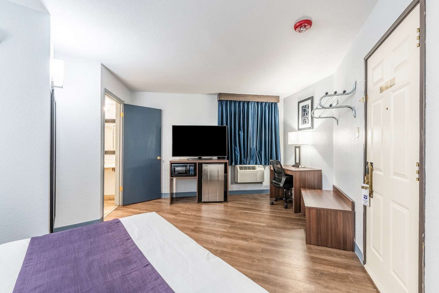 A hotel room with a bed, a desk, a television, and a door.