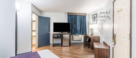 A hotel room with a bed, a desk, a television, and a door.
