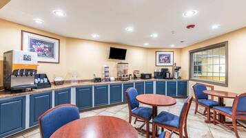 A hotel room with a kitchenette, a flat-screen TV, a coffee machine, and a seating area with chairs and a table.