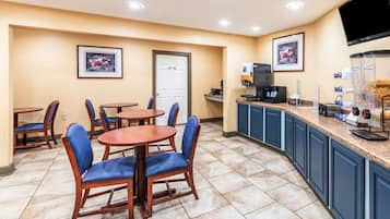 Una habitación de hotel con zona de comedor, cafetera y televisor montado en la pared.