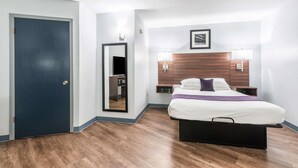 A hotel room with a bed, bedside lamps, a wooden headboard, a mirror, and a door. - Americas Best Value Inn Searcy (Searcy)