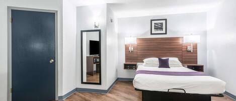 Una habitación de hotel con cama, lámparas de noche, cabecera de madera, espejo y puerta.