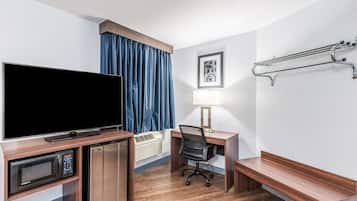 Habitación de hotel con televisión de pantalla plana, escritorio con silla, lámpara, calentador y perchero.