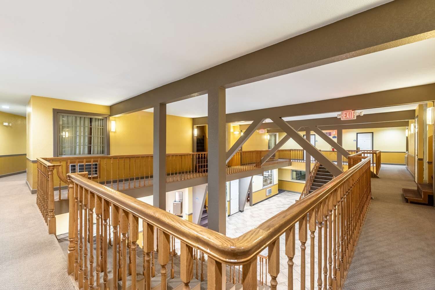A multi-level hotel interior with wooden railings, a staircase, and an exit sign.