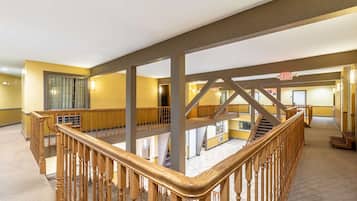 A multi-level hotel interior with wooden railings, a staircase, and an exit sign.