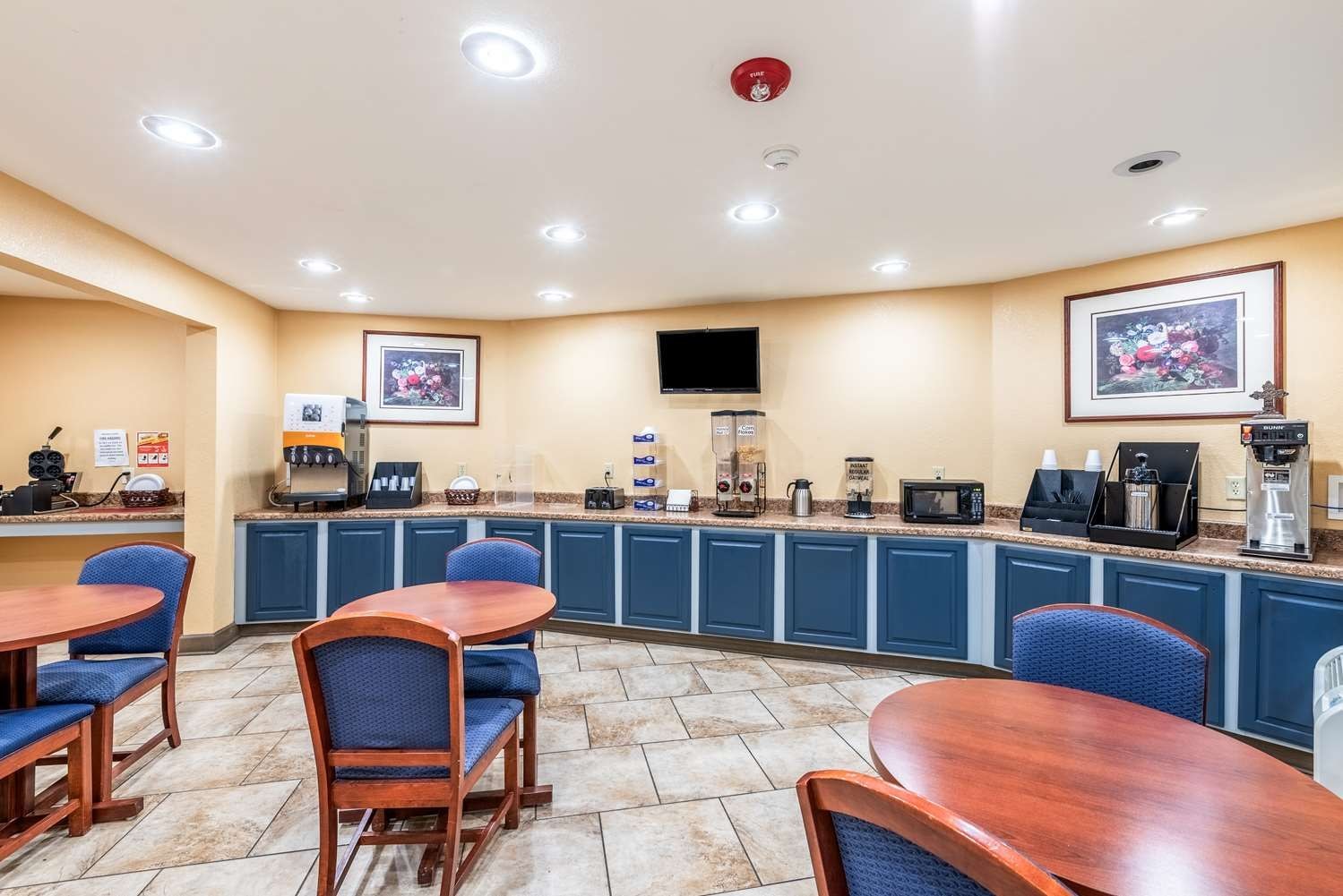 A hotel breakfast area with a counter, seating, and a mounted television.