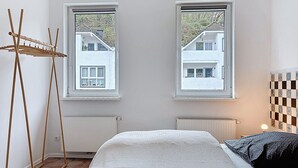 Un dormitorio con cama, dos ventanas, un radiador y un tendedero de madera.