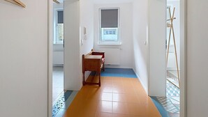 Un pasillo estrecho con un banco de madera, un radiador y una ventana con persianas.