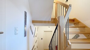 Una escalera de madera con barandillas negras que conduce a una puerta con detalles rojos.