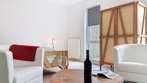 Una habitación con un sofá blanco, una mesa de madera con una botella y un vaso, y una ventana con vistas a árboles.