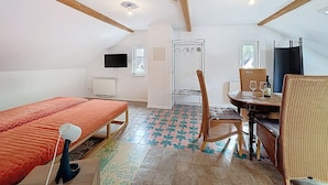 A bedroom with a bed, a chair, a table with glasses and a bottle, a TV, a radiator, and a window. - Wohnung 5 by Interhome (Sankt Goar)