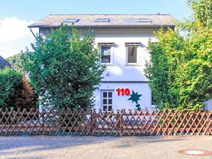 Ein weißes Gebäude mit der Hausnummer 110, umgeben von Bäumen und einem Holzzaun.