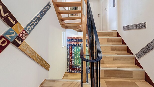 A staircase with a wooden handrail, a wall with a colorful abstract art piece, and a door at the top. - Apartmenthaus 110 by Interhome (Sankt Goar)