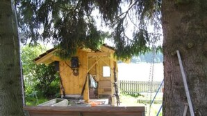 A wooden cabin with a porch, surrounded by trees and gravel.