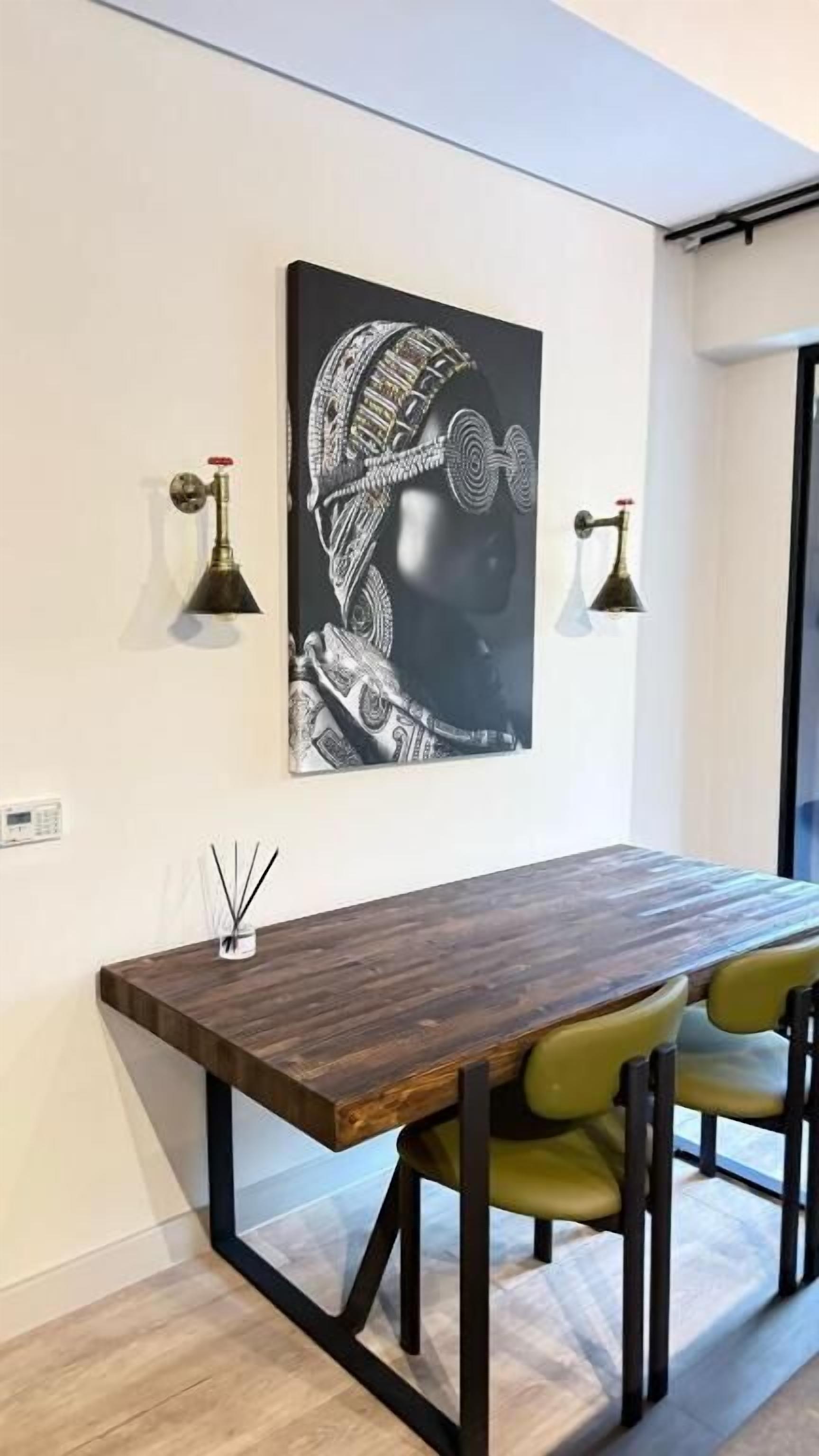 A dining area with a wooden table and chairs, a wall-mounted artwork, and two wall-mounted lamps.