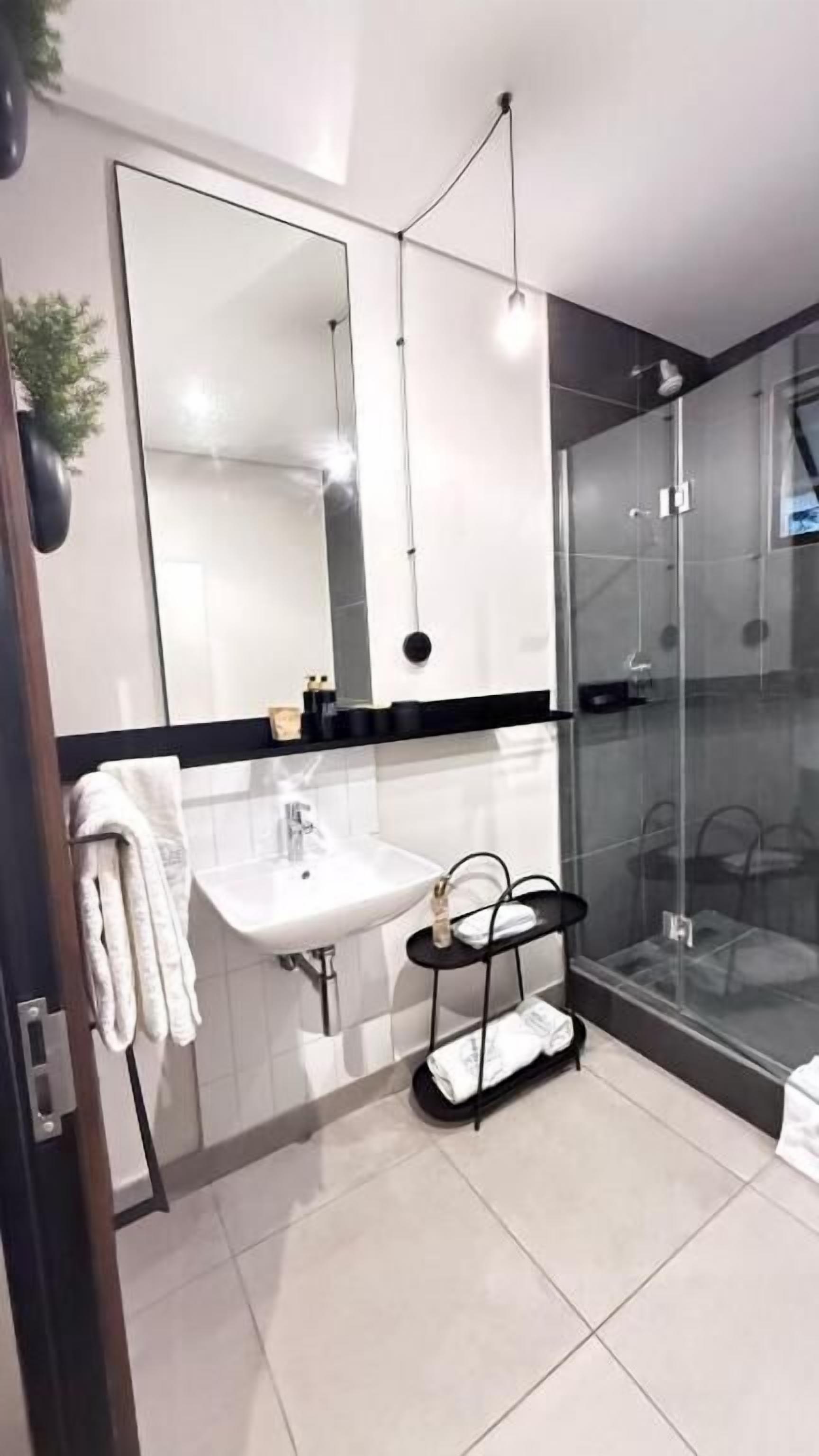 Un baño moderno con un espejo grande, un lavabo, una cabina de ducha de vidrio y un perchero para toallas.