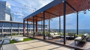 An outdoor terrace with seating, a wooden deck, and a view of a cityscape. - The Henlee Apartment Sandton (Sandton)