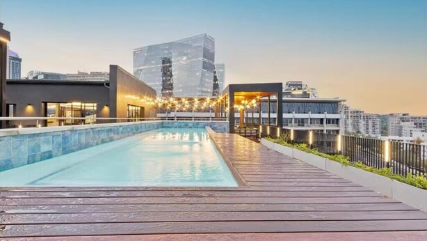 A rooftop pool with a wooden deck, surrounded by modern buildings and string lights. - The Henlee Apartment Sandton (Sandton)