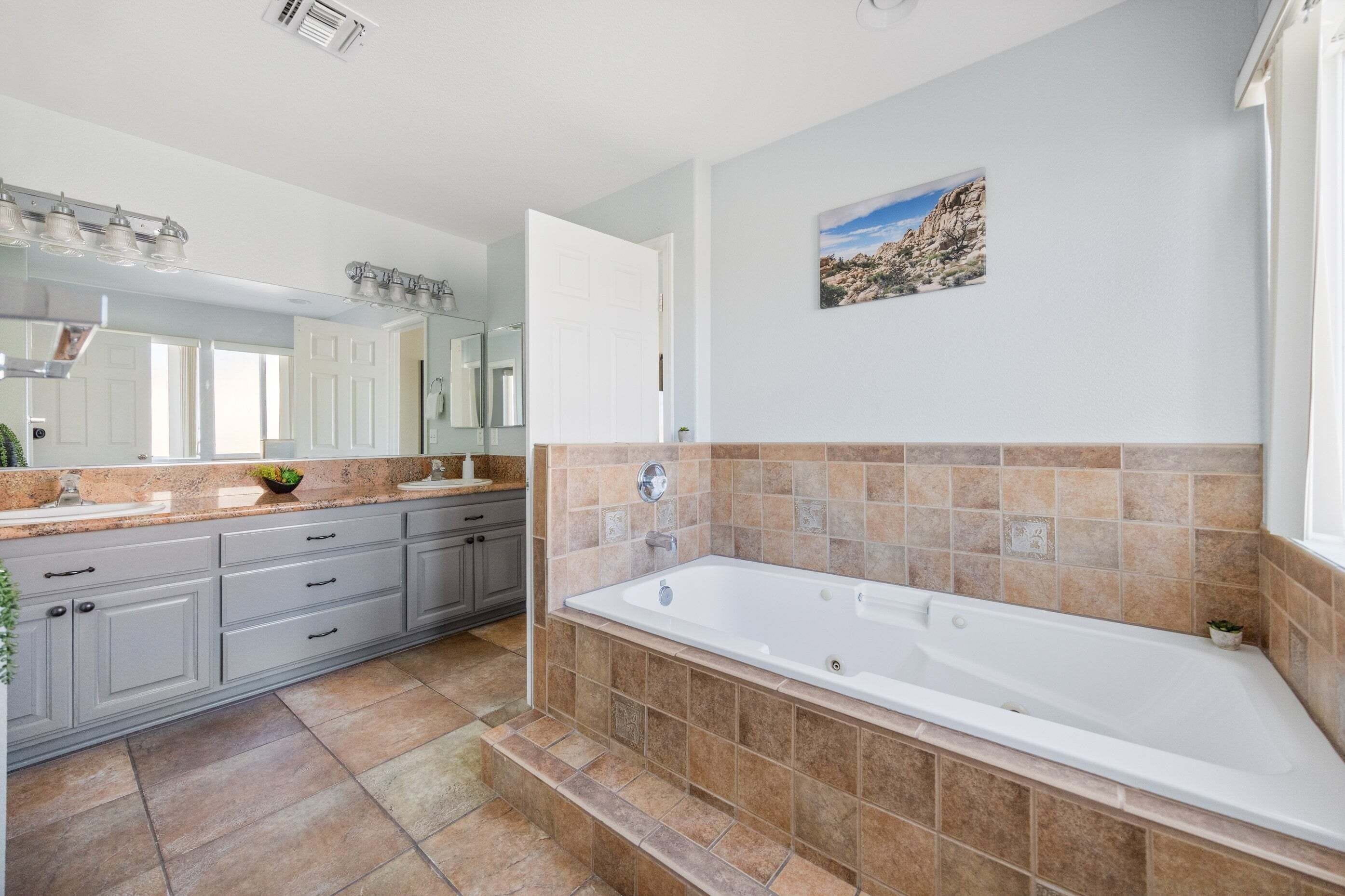 Une salle de bain moderne avec une grande baignoire, des meubles gris et un sol carrelé.