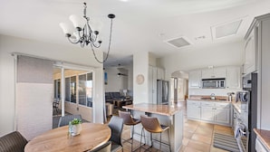 A modern kitchen with white cabinets, a central island, and a dining area with a wooden table and chairs.