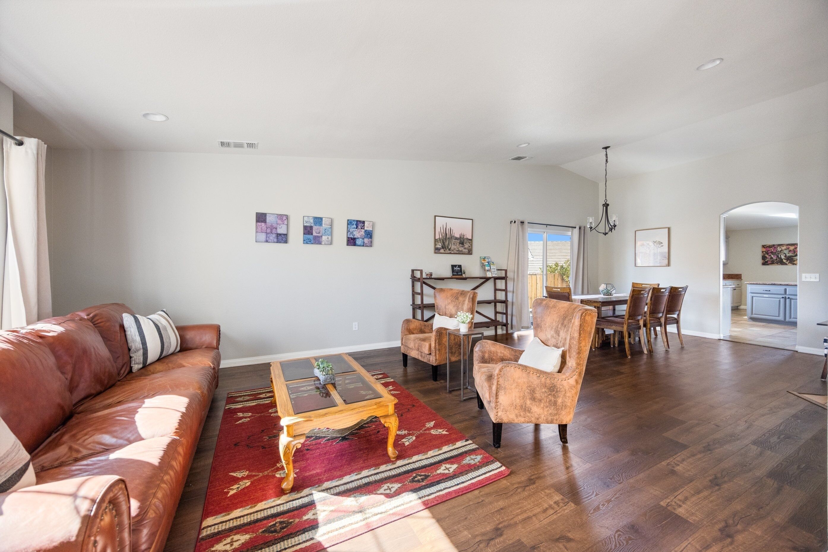 A spacious living room with a leather sofa, a coffee table, and a red rug. There is a dining area with a table and chairs in the background.