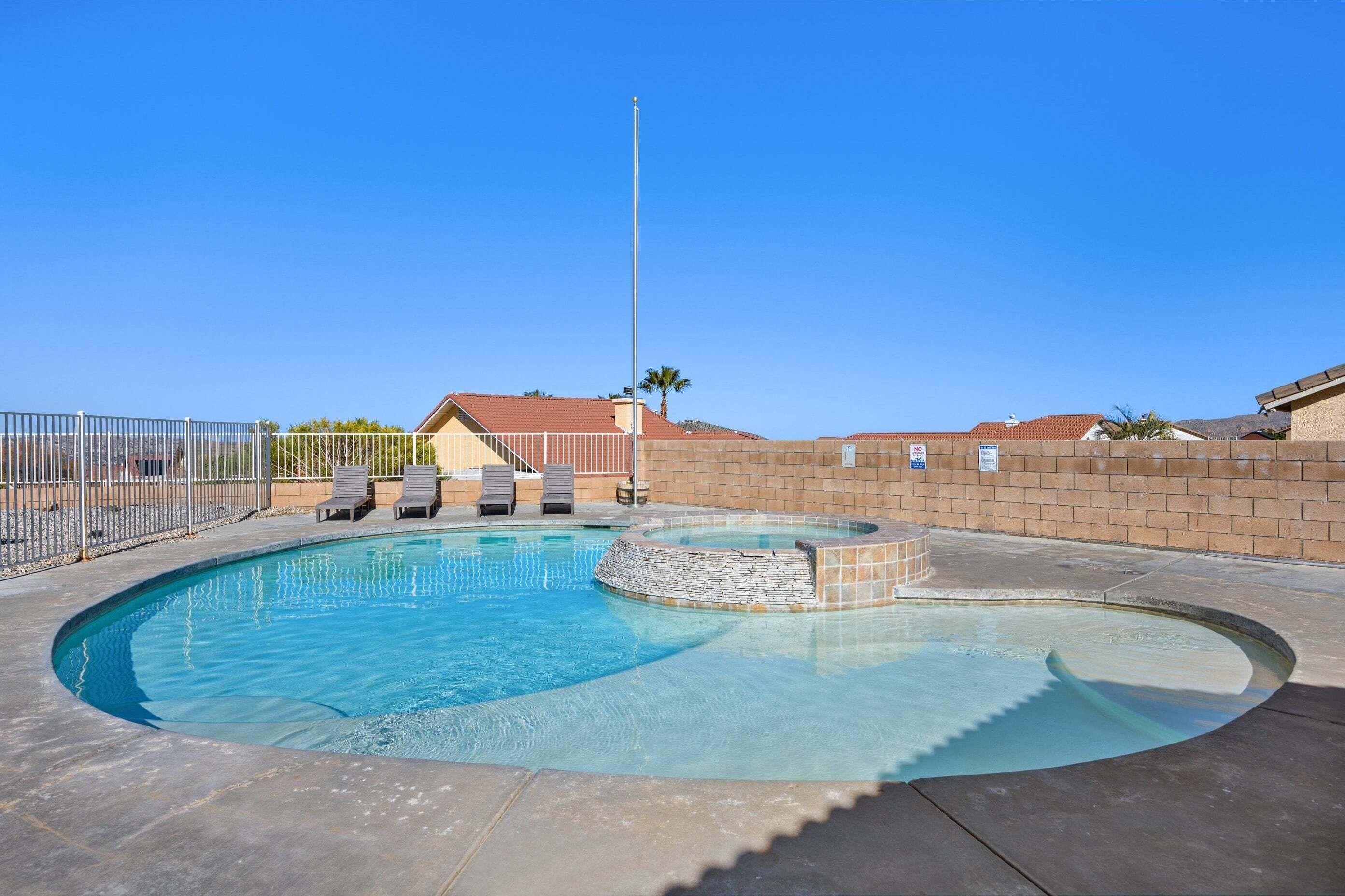 A swimming pool with a stone edge, surrounded by a brick wall and a metal fence.