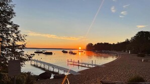 A beach with a wooden pier extending into calm waters, surrounded by trees and a sunset in the background. - Cove Overlook Limit 6 3 Bedroom Home (Standish)