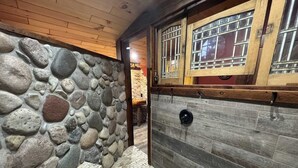 A stone wall with a wooden bench, a wooden door with barred windows, and a stone floor. - NEW! Little Ranch Therapy - Hot Tub, Fireplace (Traverse City)
