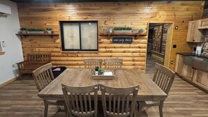 A wooden interior with a dining table and chairs, a window, and a sign that reads "cook sing dance". - NEW! Little Ranch Therapy - Hot Tub, Fireplace (Traverse City)