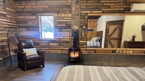 A cozy room with a wooden wall, a fireplace, a leather chair, and a bed with striped bedding. - NEW! Little Ranch Therapy - Hot Tub, Fireplace (Traverse City)