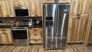 A modern kitchen with wooden cabinets, stainless steel appliances, and a built-in water dispenser. - NEW! Little Ranch Therapy - Hot Tub, Fireplace (Traverse City)