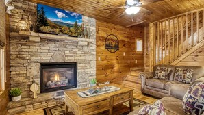 A cabin interior with a stone fireplace, wooden walls, a sofa, and a ceiling fan. - Elk Crossing 3 Bedroom Cabin (Pigeon Forge)