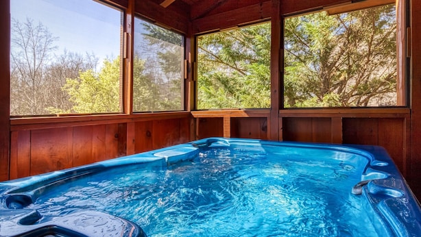 A hot tub inside a wooden cabin with large windows and a view of trees. - Elk Crossing 3 Bedroom Cabin (Pigeon Forge)
