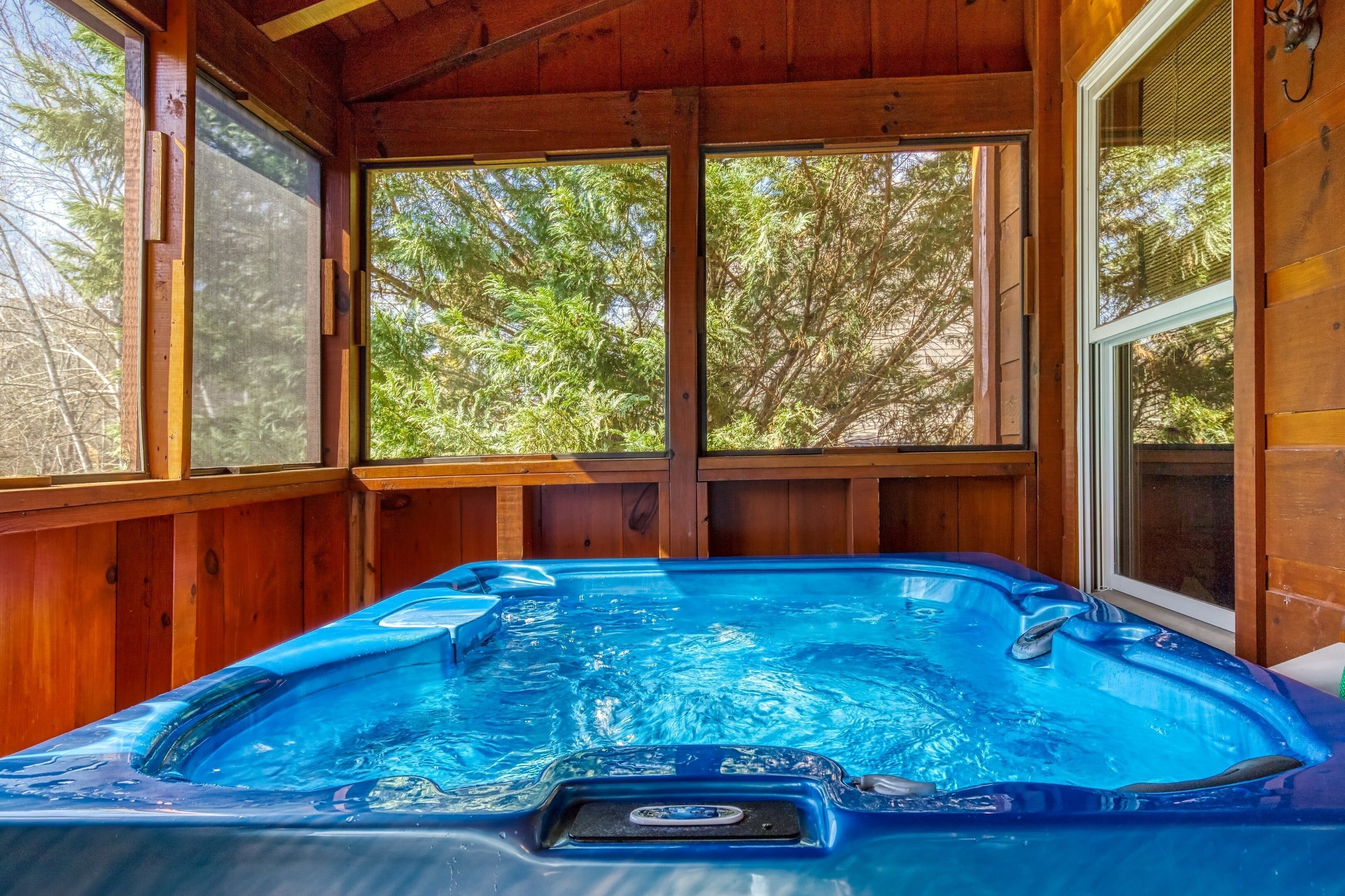 A hot tub in a wooden cabin with large windows and a view of trees.