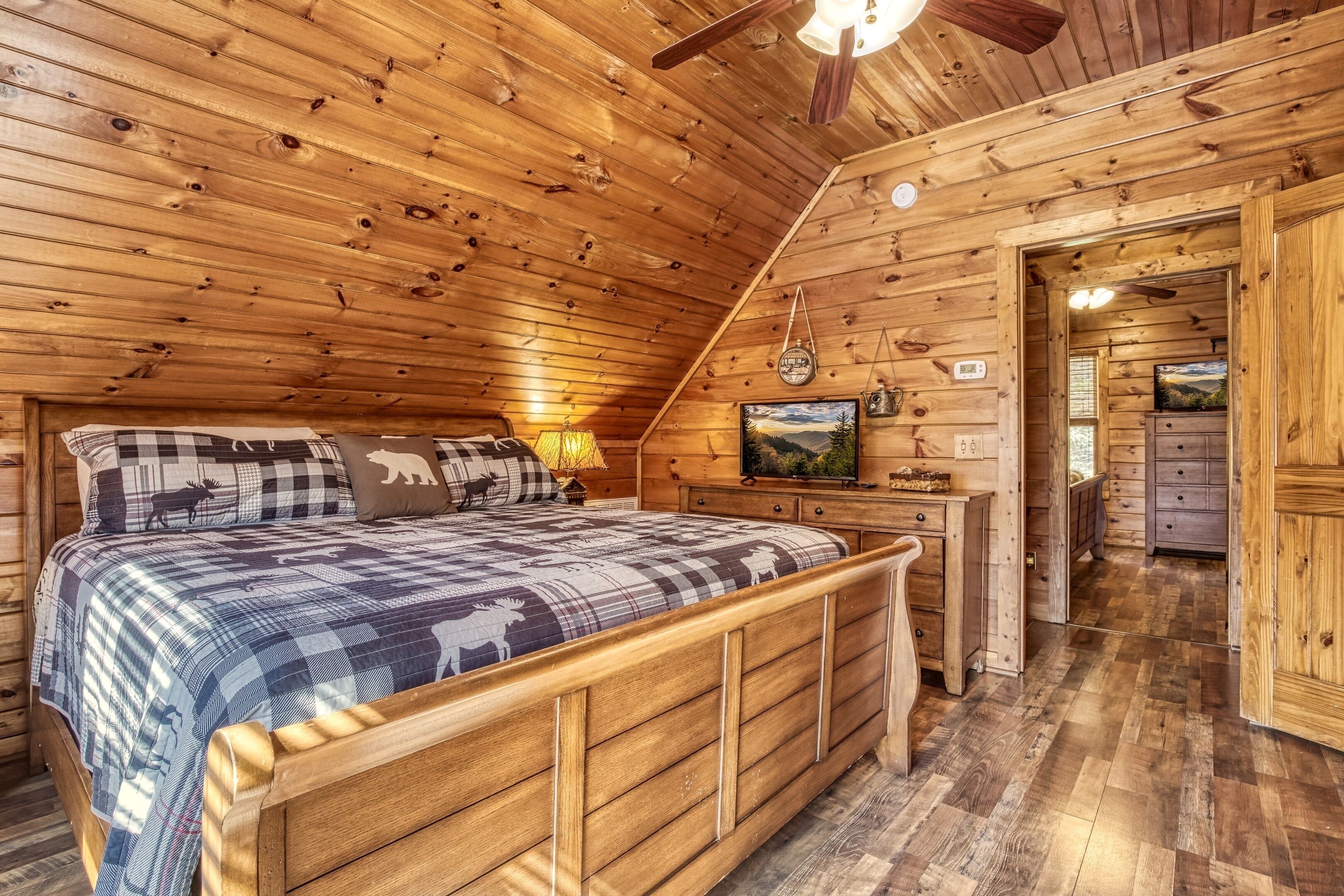 A wooden cabin bedroom with a bed, a desk, and a television.