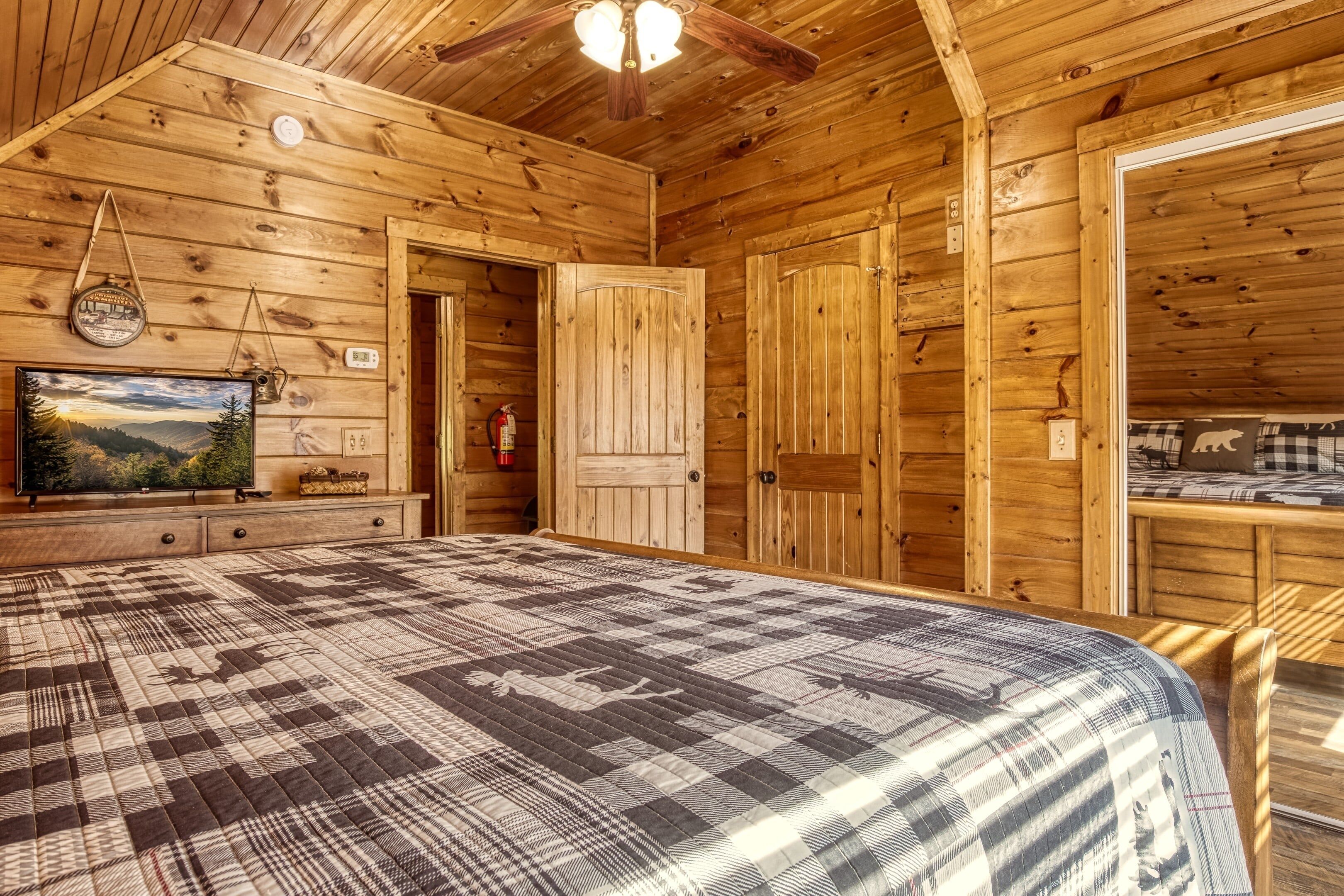 A wooden cabin interior with a large bed, a television, and a fireplace.