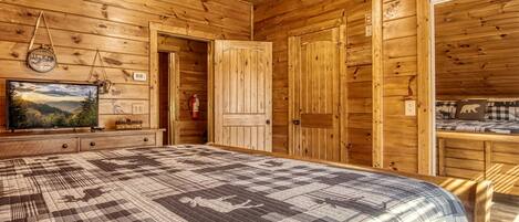 A wooden cabin interior with a large bed, a television, and a fireplace.