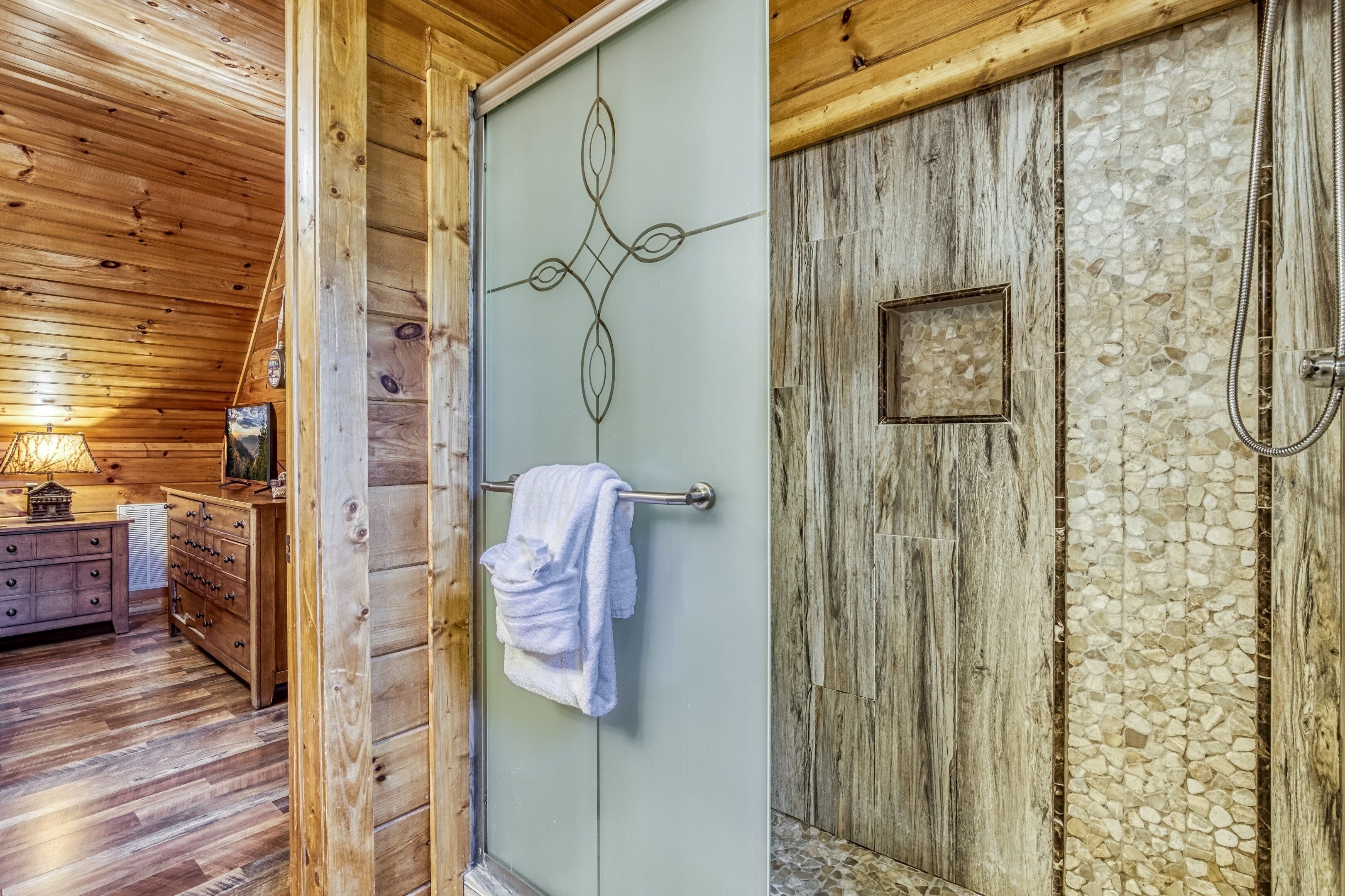 A wooden interior with a shower area featuring a mosaic wall and a towel hanging on a door.