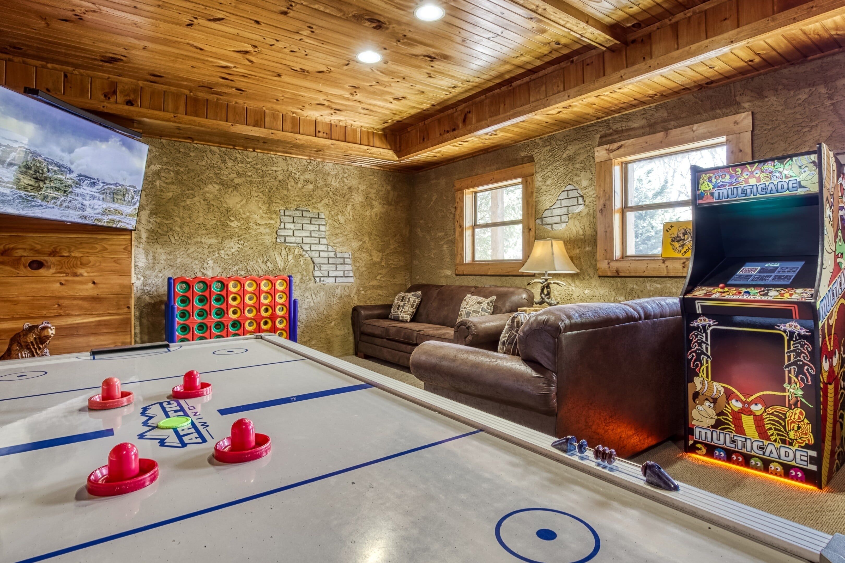 Une pièce avec une table de baby-foot, un canapé, un mur en briques et une borne d’arcade Multicade.