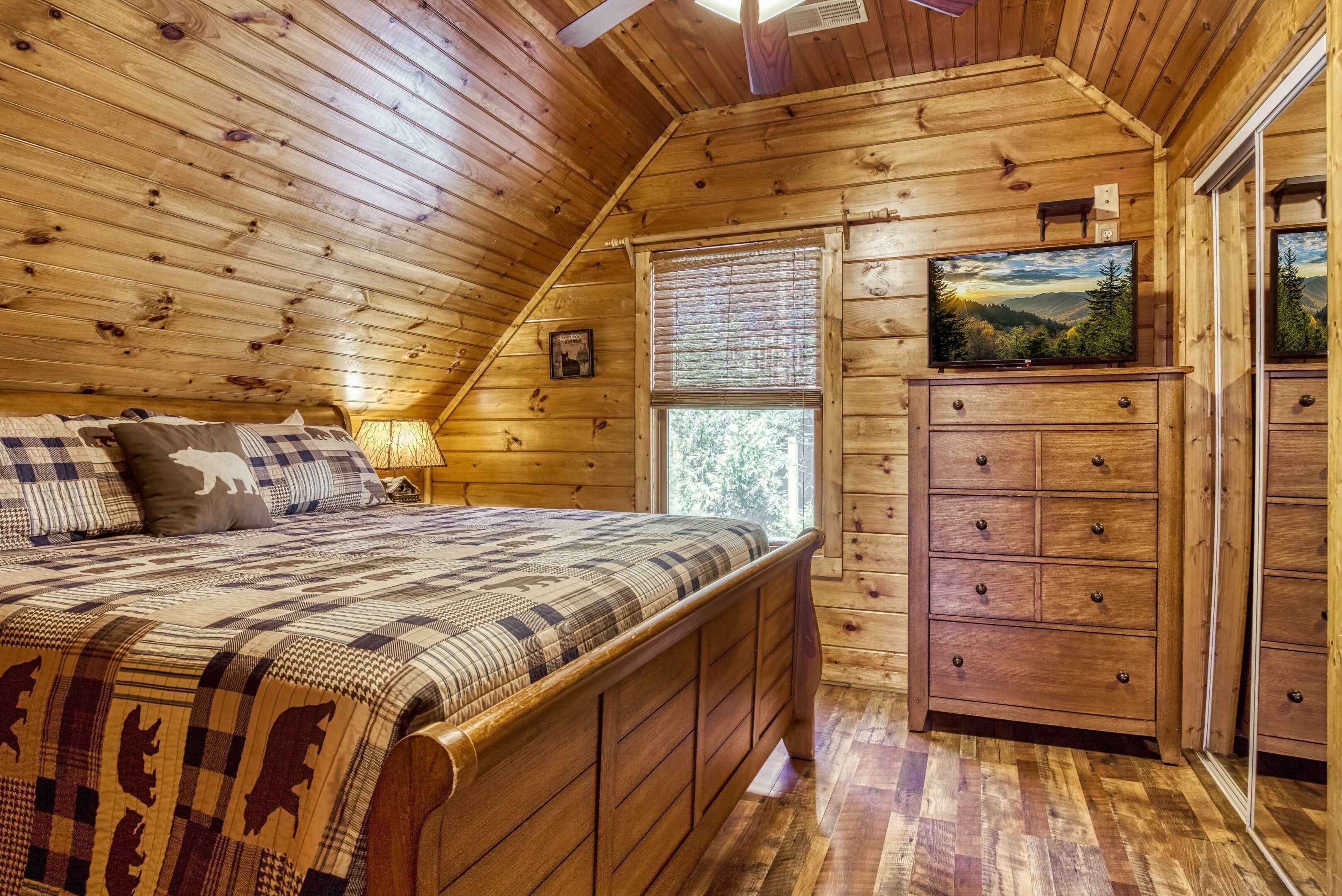 A wooden cabin bedroom with a bed, dresser, and a TV on the wall.