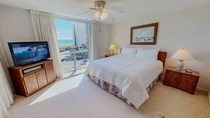 Habitación de hotel con cama, televisión, un cuadro, lámpara y vista a la playa.